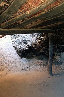 Upper Cliff Dwelling Room 4. A reed ceiling with horizontal wood beams is supported by a wooden pole.