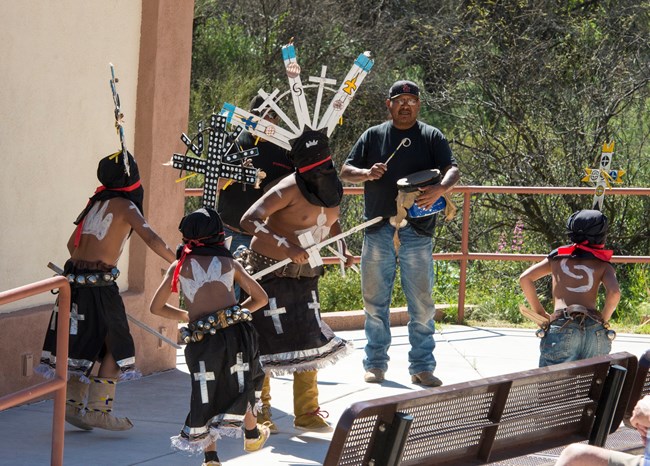 Four dancers in an amphitheater with two drummers in the background.