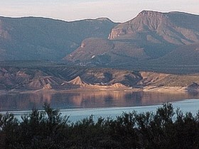 Roosevelt Lake with vegetation in front and mountains in the background.