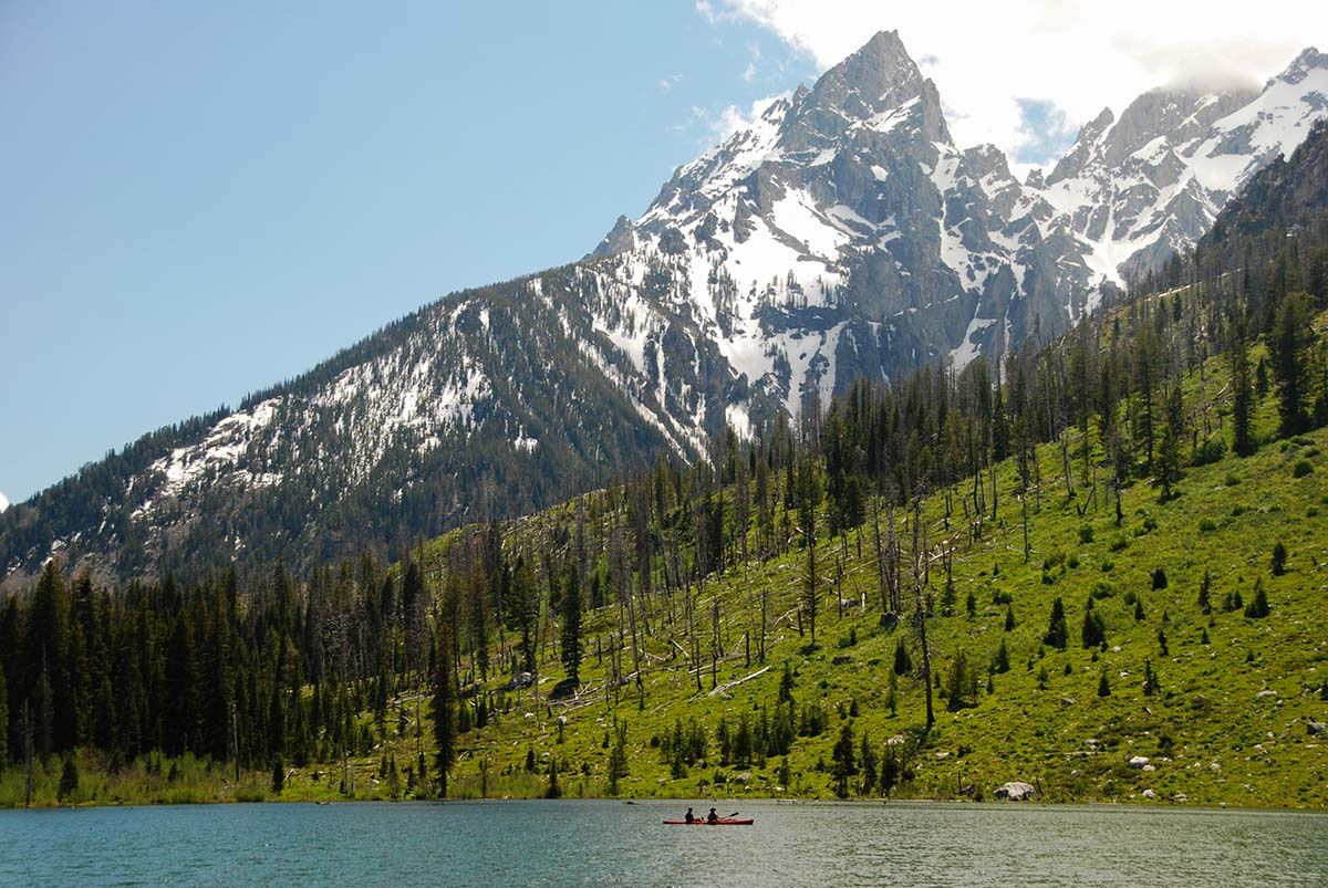 A kayak floats in a turquoise lake at the base of jagged mountain peaks.