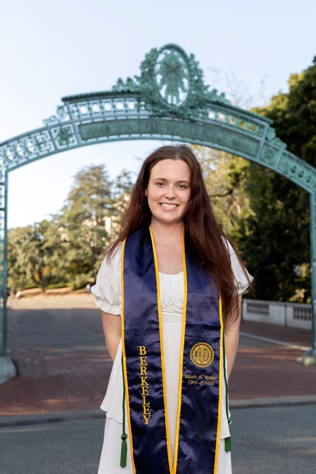 A woman stands in her graduation regalia.