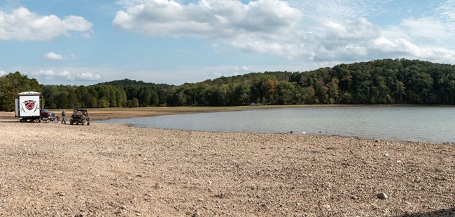 An RV sits along the shore of a lake.