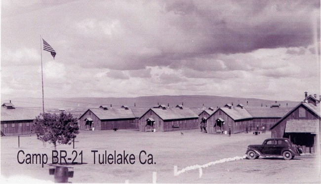A row of barracks buildings behind a field with an American flag