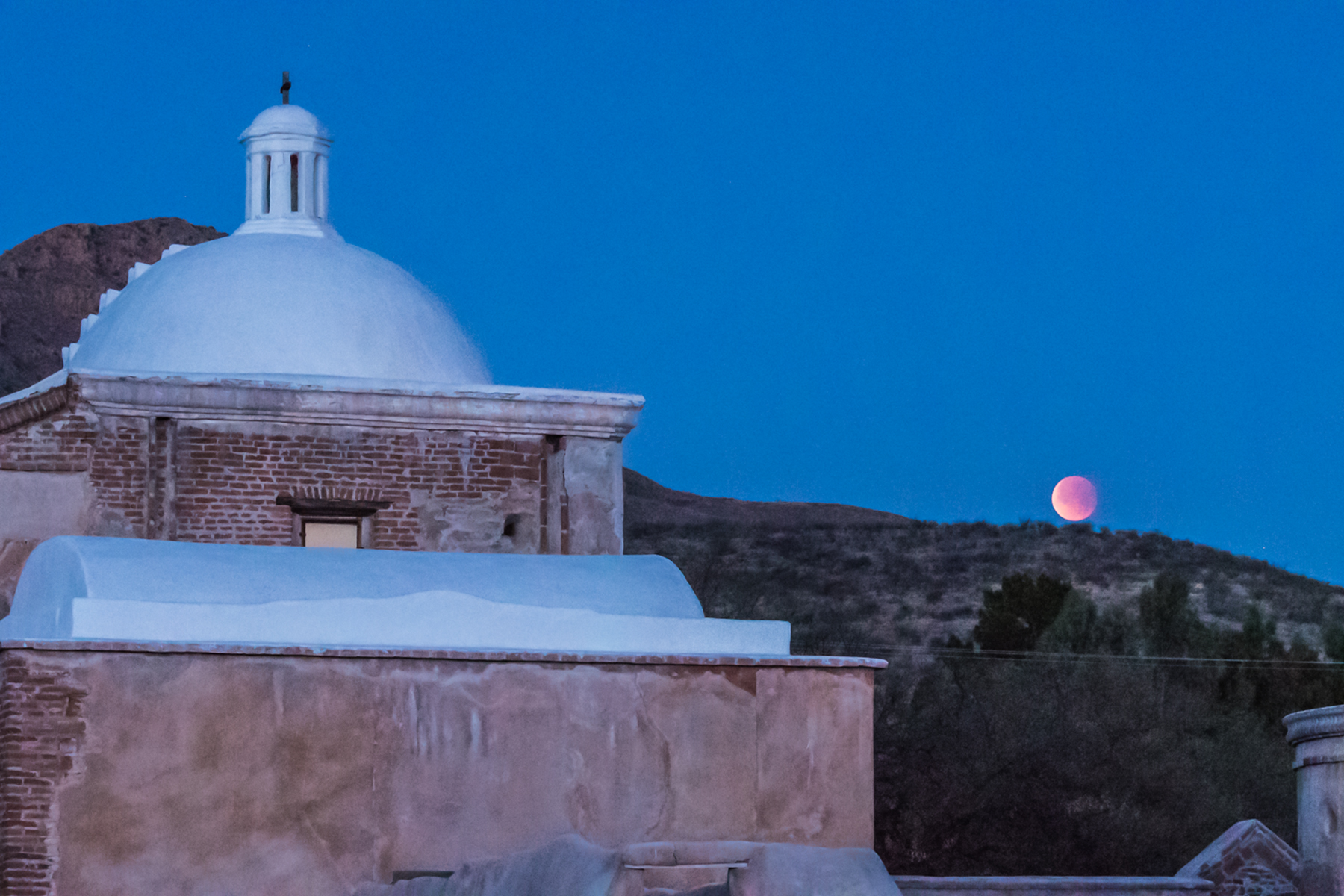 Night image of adobe church with full moon in the background.