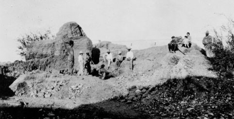 historic photo of people sitting on low adobe wall ruins