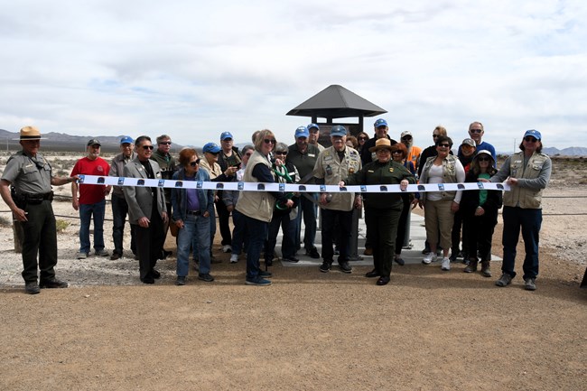 A group of park rangers and Protectors of Tule Springs cut a ribbon near a trailhead kiosk