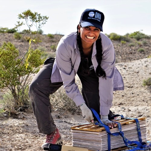 A woman smiles at the camera and pulls the straps on a plant press.