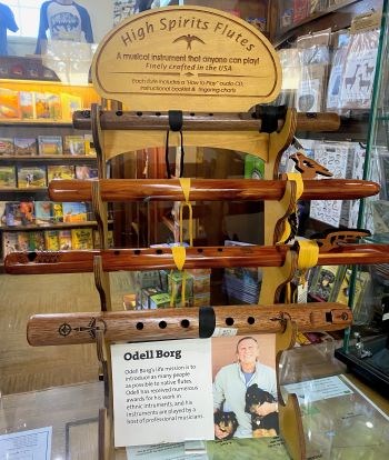A display rack of wooden flutes with different designs and a sign for High Spirits Flutes featuring an image of a bird
