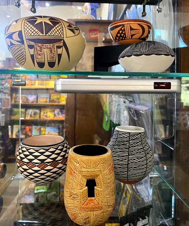 several small, clay pots of varying shapes with different black and brown designs painted on them in a glass display case