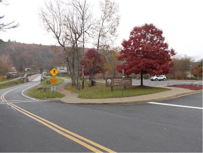 paved road leads onto bridge. To the right of the road is a paved parking area. A sign next to the parking area reads "Roebling's Delaware Aqueduct."