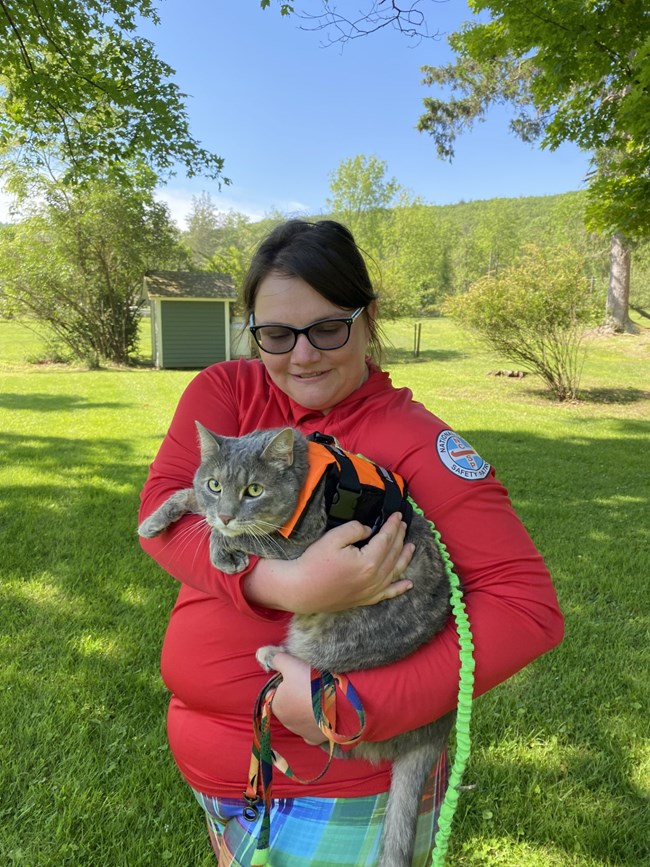Lady wearing NCSp volunteer shirt holding a cat on a harness/leash