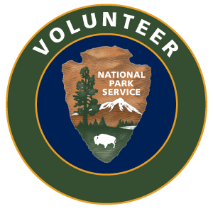 The circular National Park Service volunteer program logo with an arrowhead inside of a green ring that says "Volunteer."