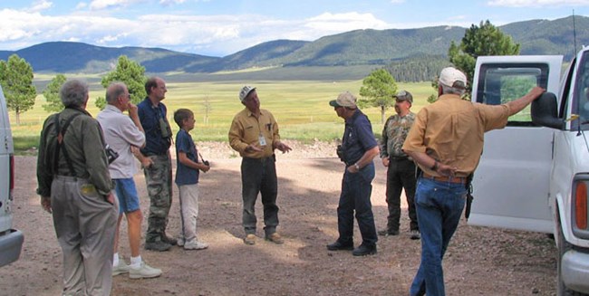 Adults and children listen to a ranger backed by scenic valley and mountains.