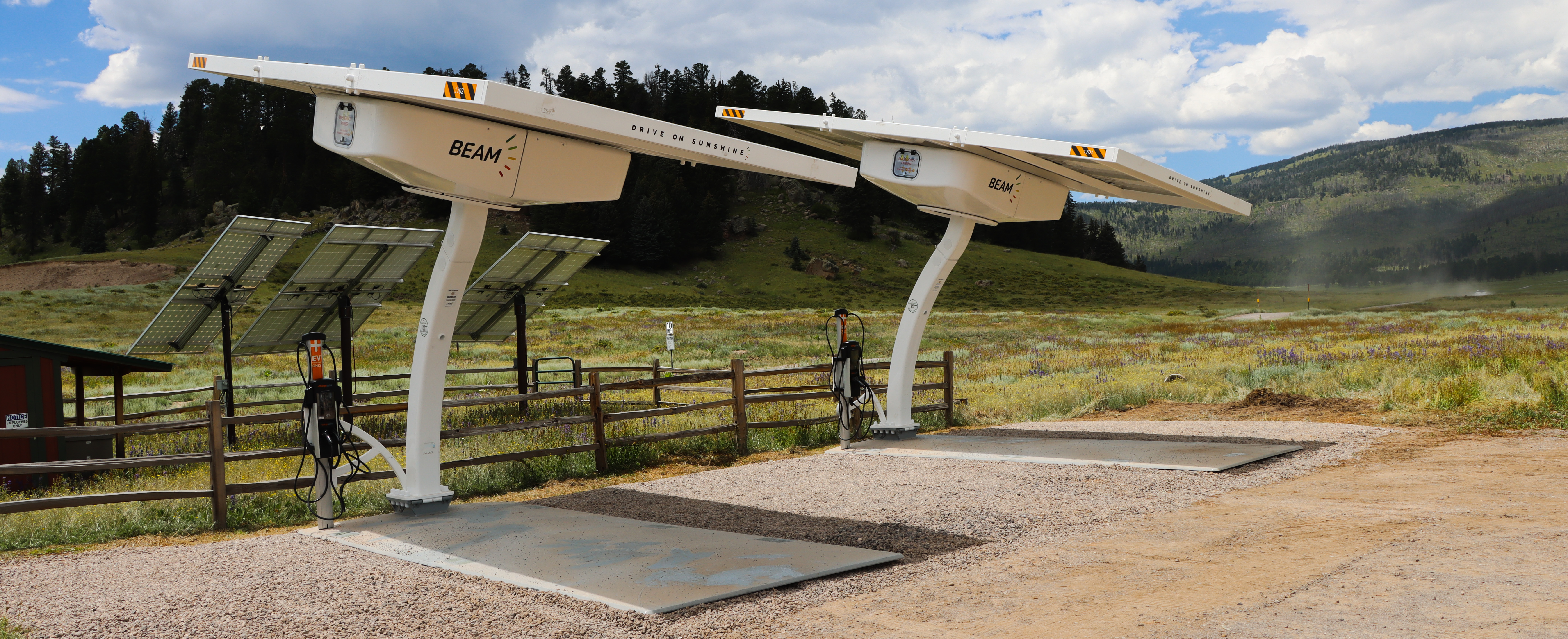 Two solar-powered electric vehicle charging stations in a gravel parking lot.