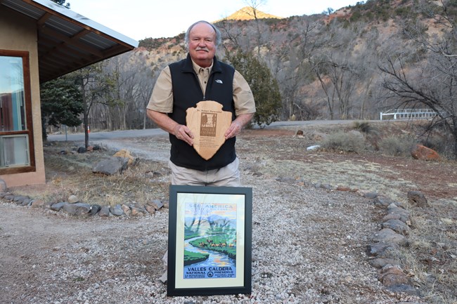 A man holds a wooden arrowhead-shaped plaque while standing outside of an office building.