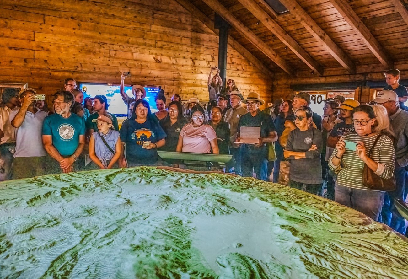 A crowd of people gather around a large, circular, 3D map of a caldera.