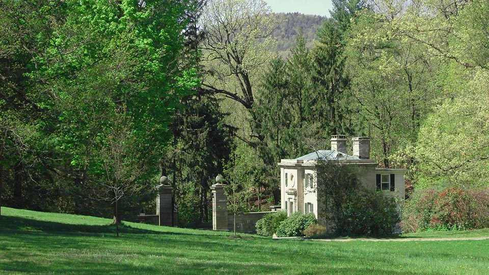 A limestone building near a gate and surrounded by green lawn.