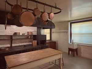 A kitchen with large coal stove and hanging copper pots.