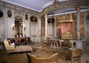 A room with French gild furnishings and a bed surrounded by an architectural railing.