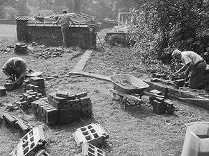 Three men laying brick walls in a garden.