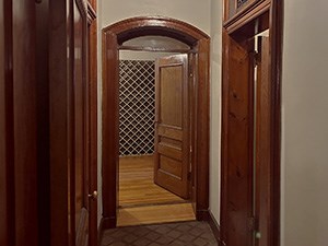 A small vestibule with doors on each wall, one door open to reveal an empty wine rack.