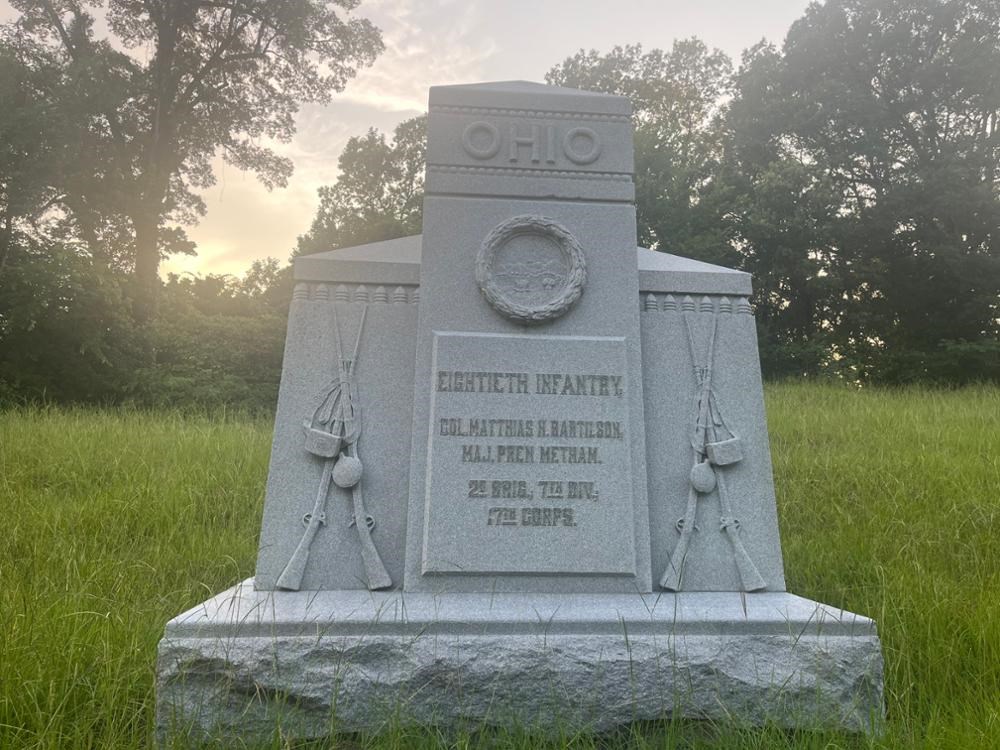 Stone Monument with stacked rifled muskets and minie ball decoration on either side of central column, which reads: OHIO Eightieth Infantry/ Col. Matthias H. Bartilson, Maj. Pren Metham./2d Brig., 7th Div., 17th Corps.