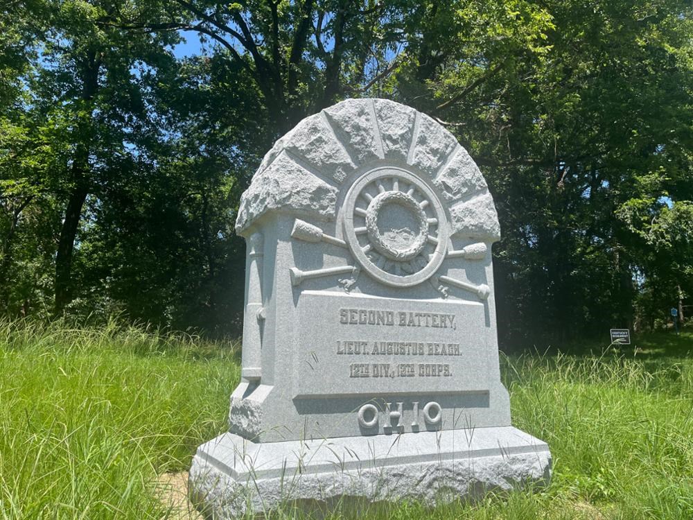 Stone Monument with rounded top, featuring a spoked wheel and crossed sponge rammers. Inscription reads: Second Battery. Lieut. Augustus Beach./12th Div., 13th Corps./OHIO