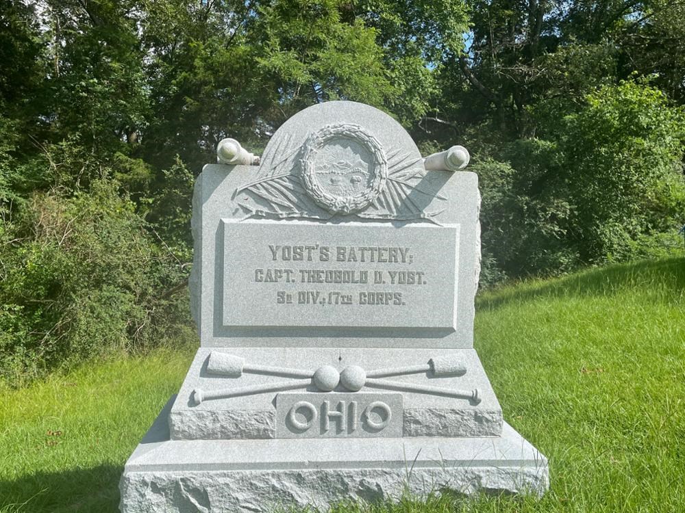 Stone Monument with rounded top and carved cannon. Two cannonballs sit at the center of two crossed sponge rammers. Inscription: Yost's Battery; / Capt. Theobold Yost. / 3d Div., 17th Corps / OHIO