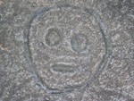 a closeup of a Taino petroglyph, showing a circular face enclosing 2 empty circular eyes and an oval mouth