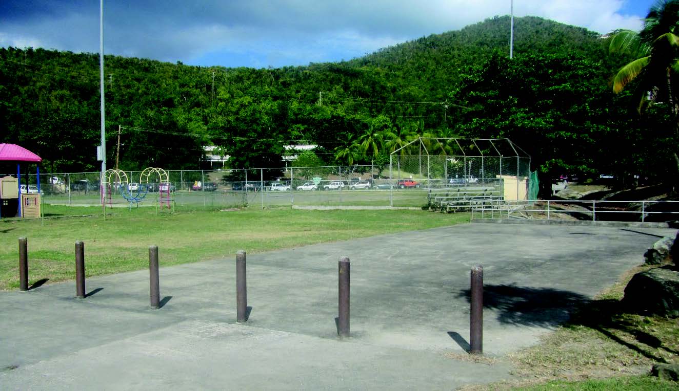 Brown bollards mark off a concrete pad in front of a playground and fenced-in ballfield