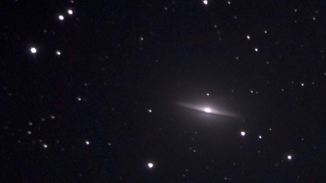 A photo of the Sombrero Galaxy shows a streak of blight light surrounded by the dark backdrop of space peppered with individual stars in the foreground.