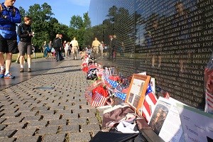 People looking Vietnam Veterans Memorial wall with flags and mementos in front