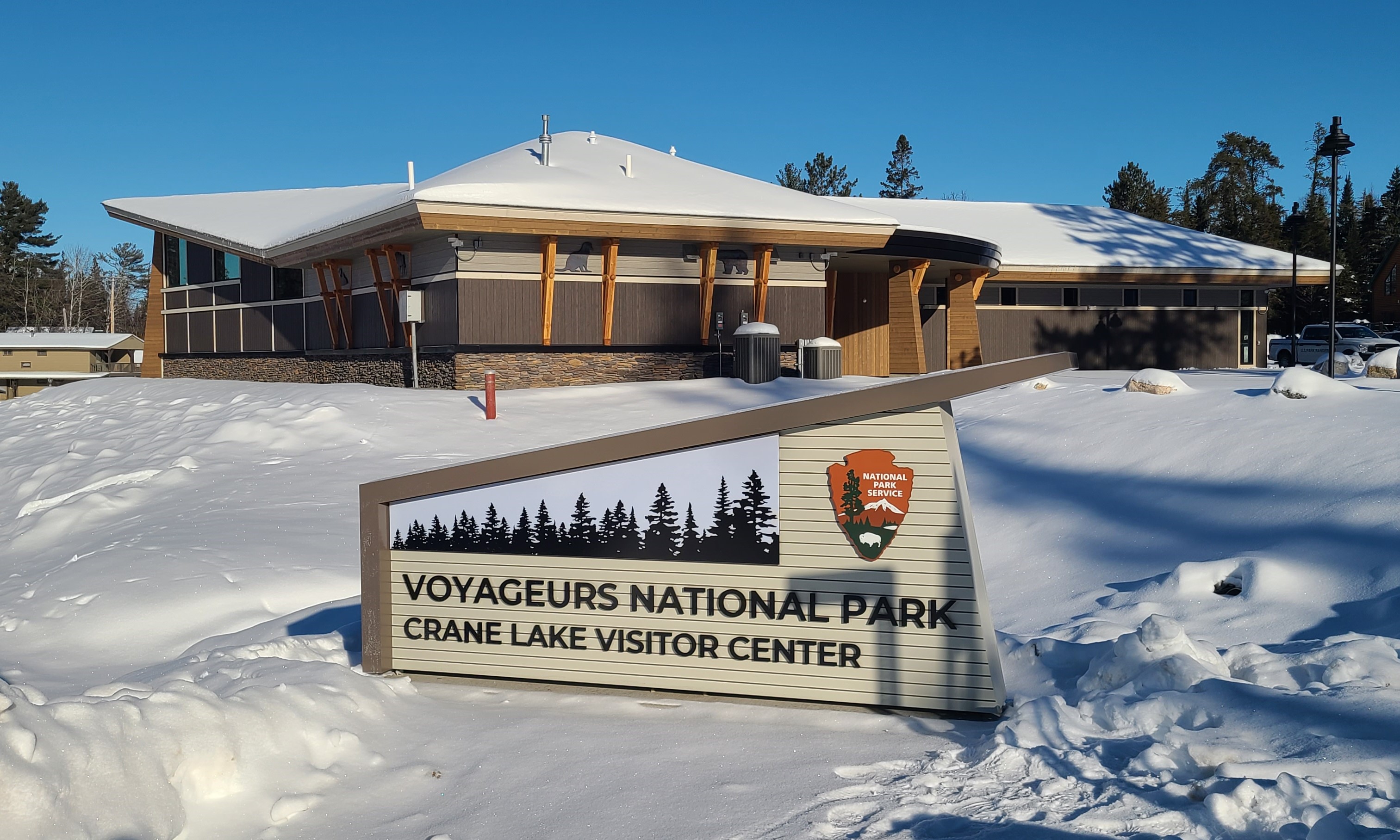 Crane Lake Visitor Center sign with the building in the background in the wintertime with deep snow on the ground under a bright blue sky.