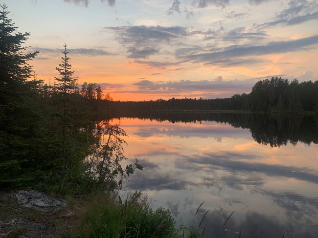 A sunset on the tree-lined horizon of a scenic lake