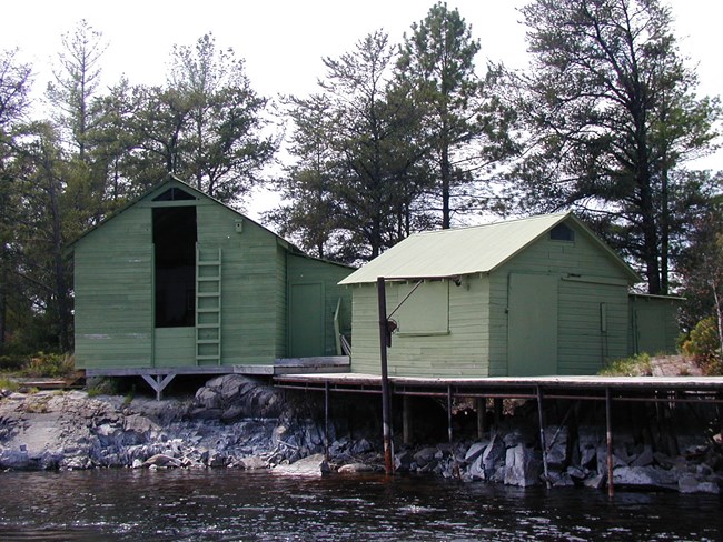 Two historic structure in park, one has a large opening that was used to put ice blocks in, the other is a small cabin like structure that was used for fish cleaning. Dock located in front of structures.