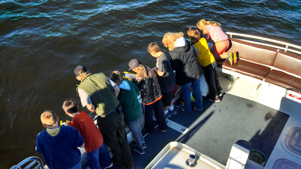 Youth with ranger looking over the side of the boat at the water