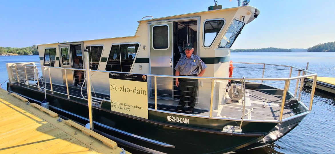 ranger in green and grey uniform greets passengers on the deck of a tour boat