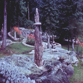 A small chair made out of stone sits atop a pillar of rock, with beds of orange lilies in the background.