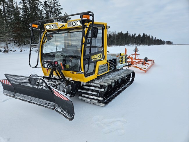 yellow snow groomer equipment on tracks grooming snow on a frozen lake.