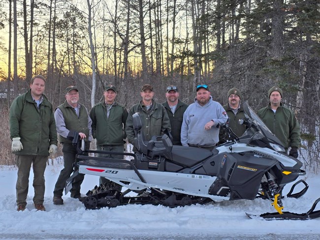 The rainy lake trails crew stands in front of a donated snowmobile