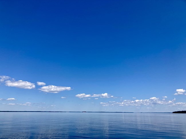 A line of white clouds is reflected brightly on the still waters of a scenic lake.