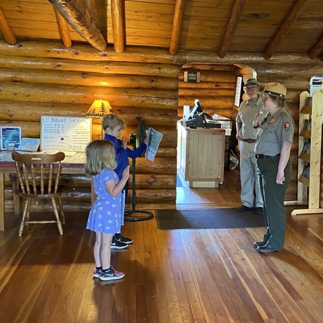Two children stand in front of a uniformed ranger with their hands raised for the jr range pledge.