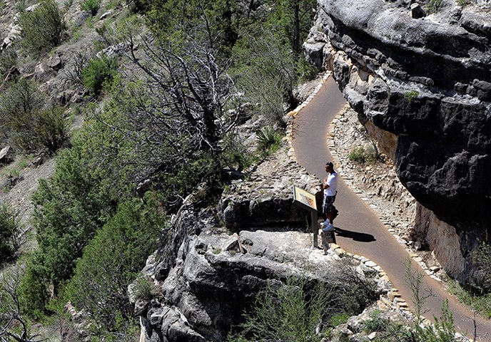 A lone visitor gazes out over Walnut Canyon from a park trail beneath the rim