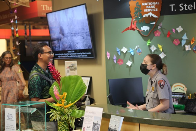 A women in a National Park Service uniform talks to a man from behind a desk.