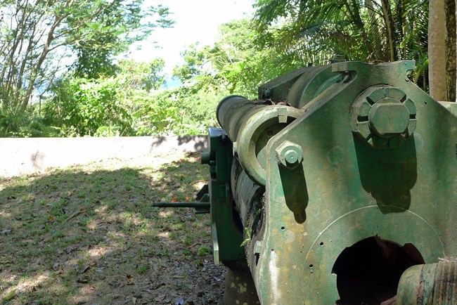 A large gun located behind a low concrete wall.