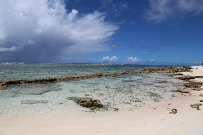 A sandy beach with large rocks just offshore.
