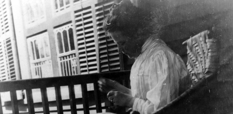 A black and white photo of a women sitting in a chair sewing.