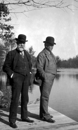 A black and white photo of two men standing on dock in winter.