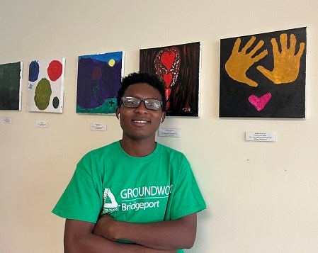 A boy in a green t-shirt stands in front of several art pieces on a wall.