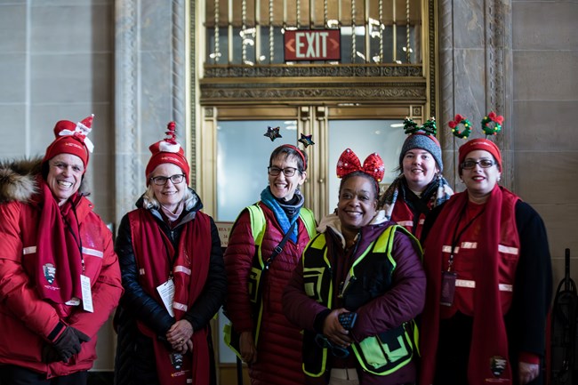 A group of six WHHO Volunteers at the White House Visitor Center dressed in red for the National Christmas Tree Lighting event
